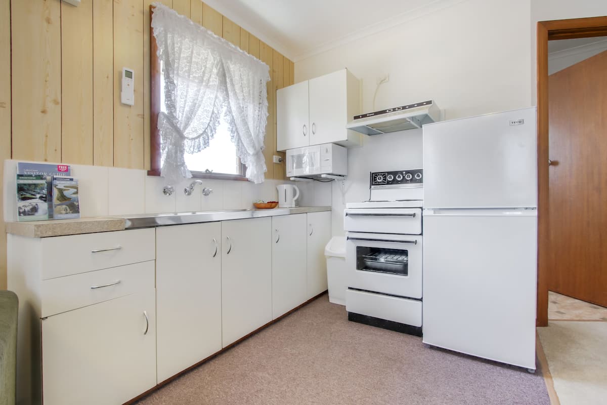 A compact kitchen with white cabinets, a microwave, a stove, and a refrigerator.