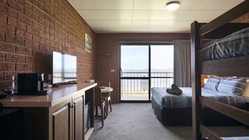 A room with a brick wall, a desk with a computer and a coffee maker, a bunk bed with blue bedding, and a large window with a view.