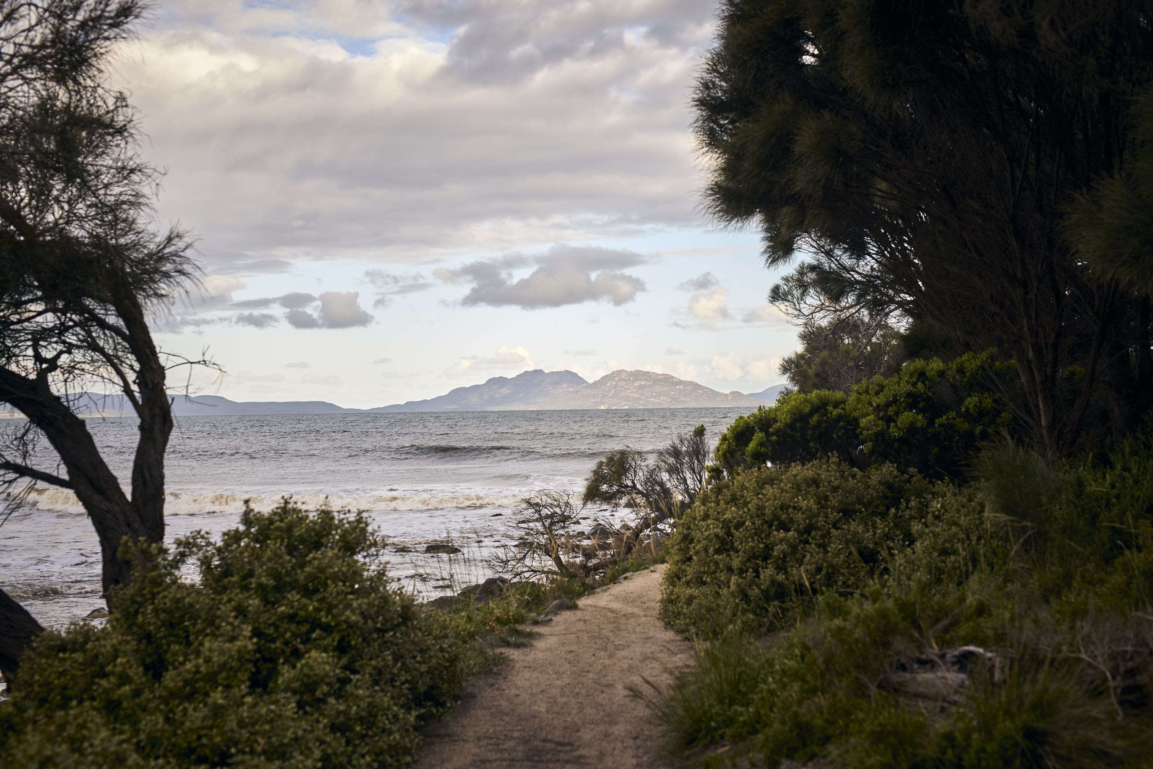 A coastal path with a view of the sea and distant mountains.