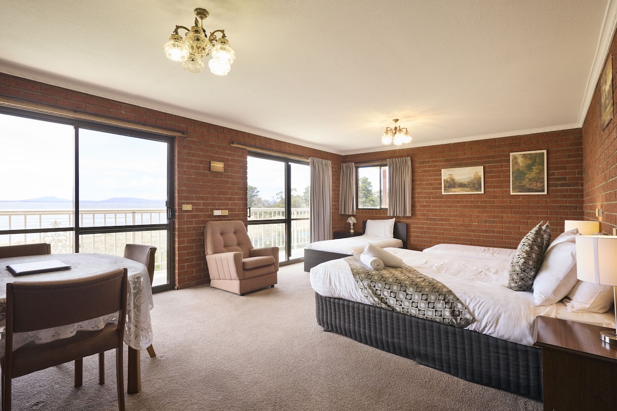 A hotel room with a large bed, a chair, a table, and a view through the window.