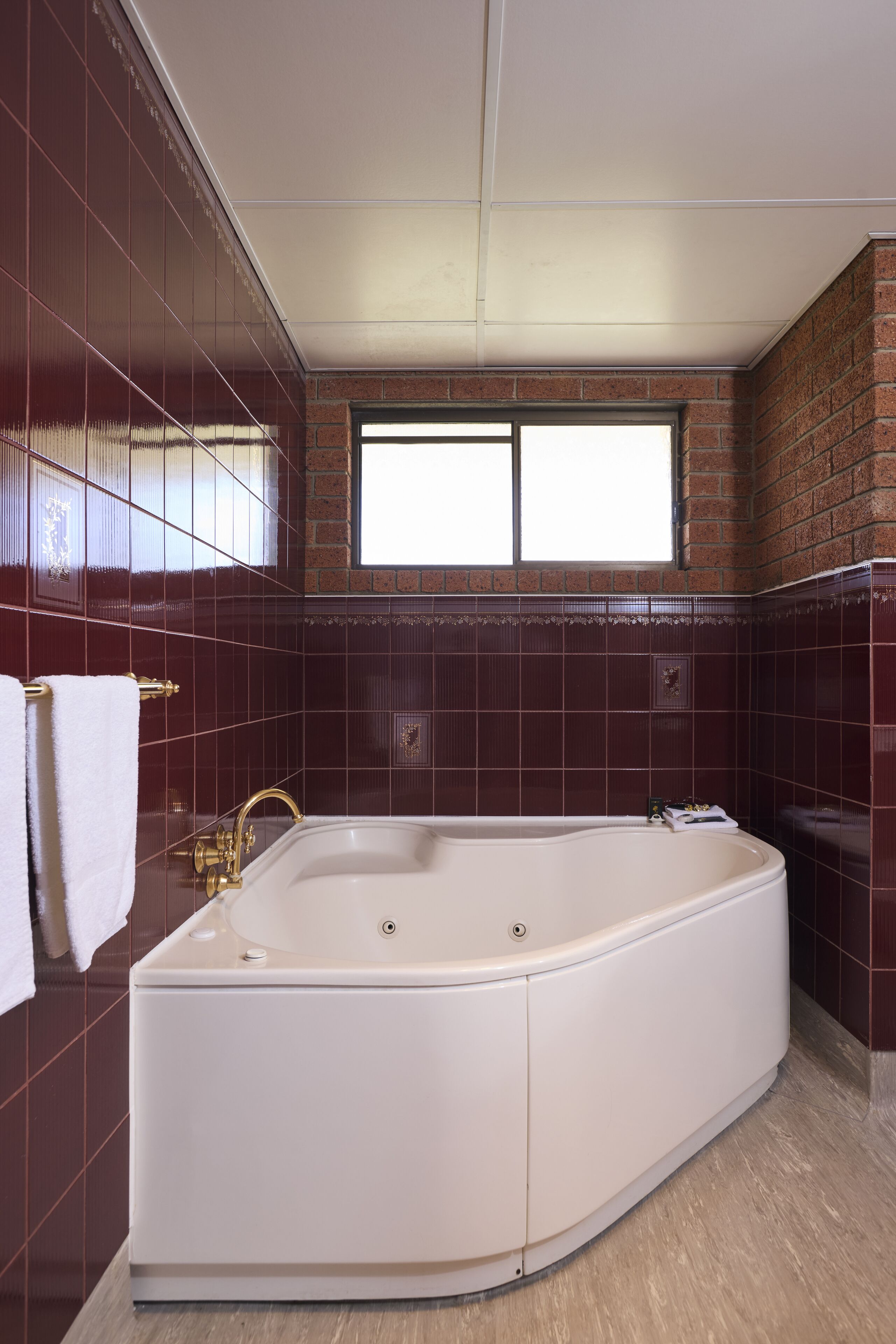 Un bagno con una grande vasca da bagno bianca, una finestra e pareti rivestite di piastrelle rosse.