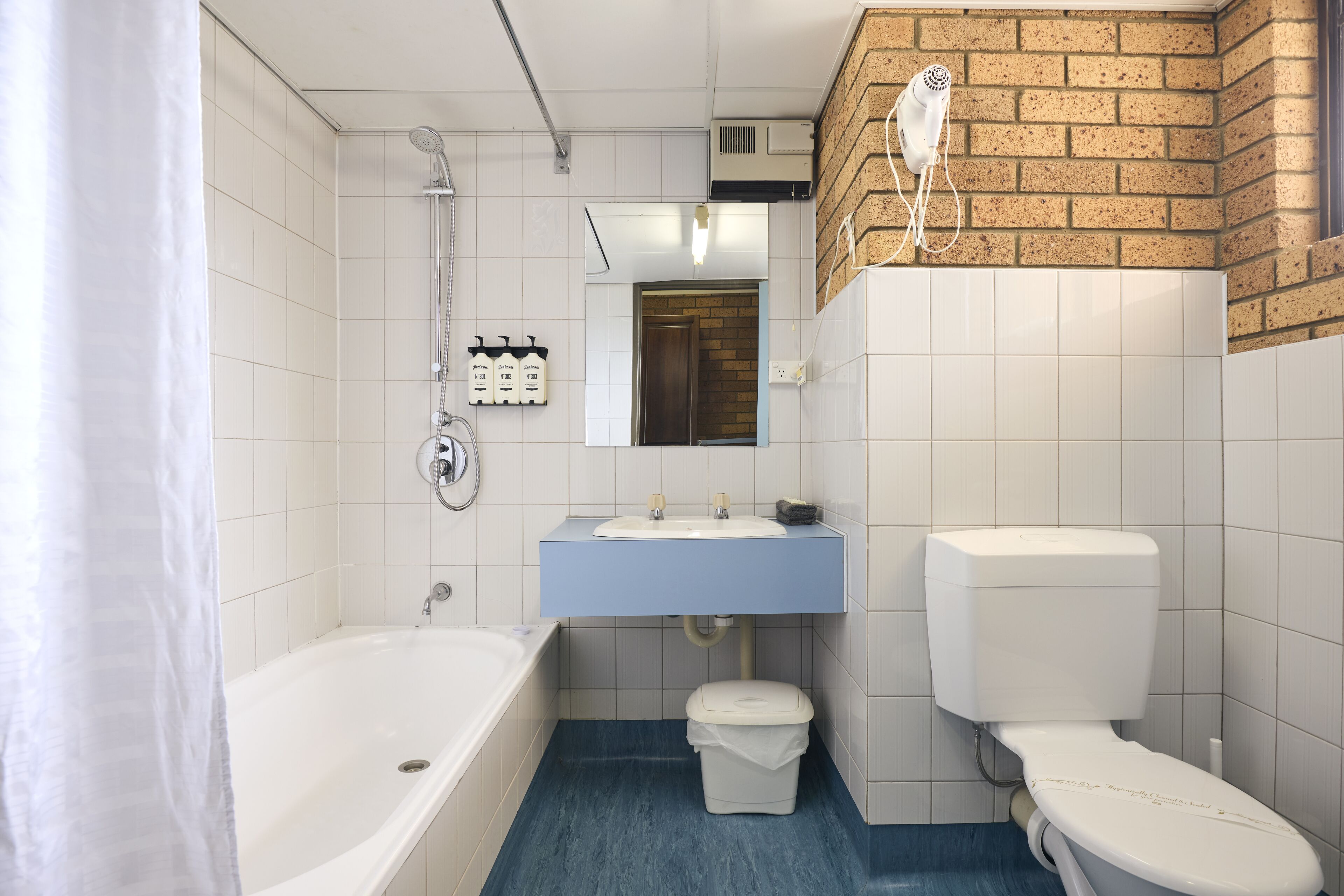 A bathroom with a bathtub, sink, toilet, and a hairdryer mounted on the wall.