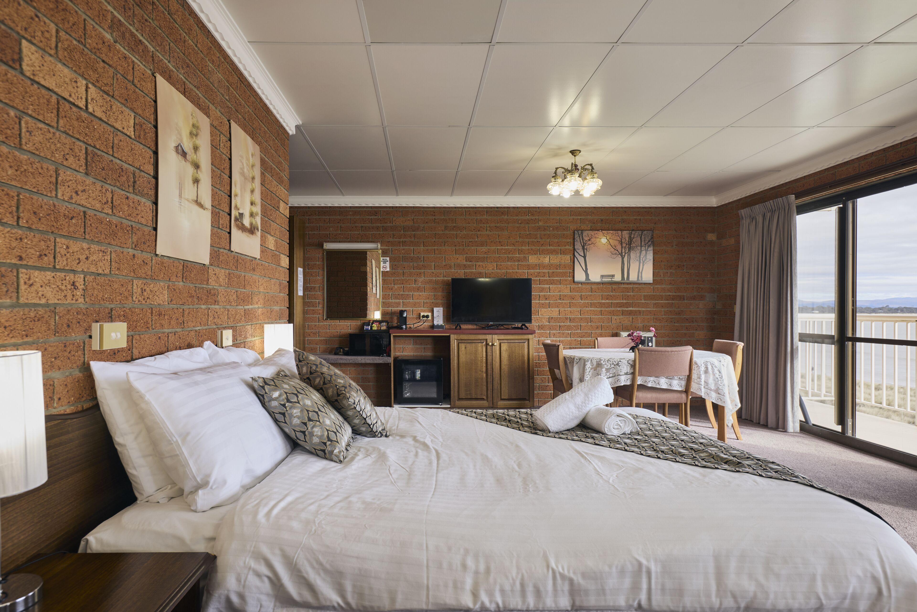 A hotel room with a large bed, a TV, a desk with a chair, and a balcony with a view.