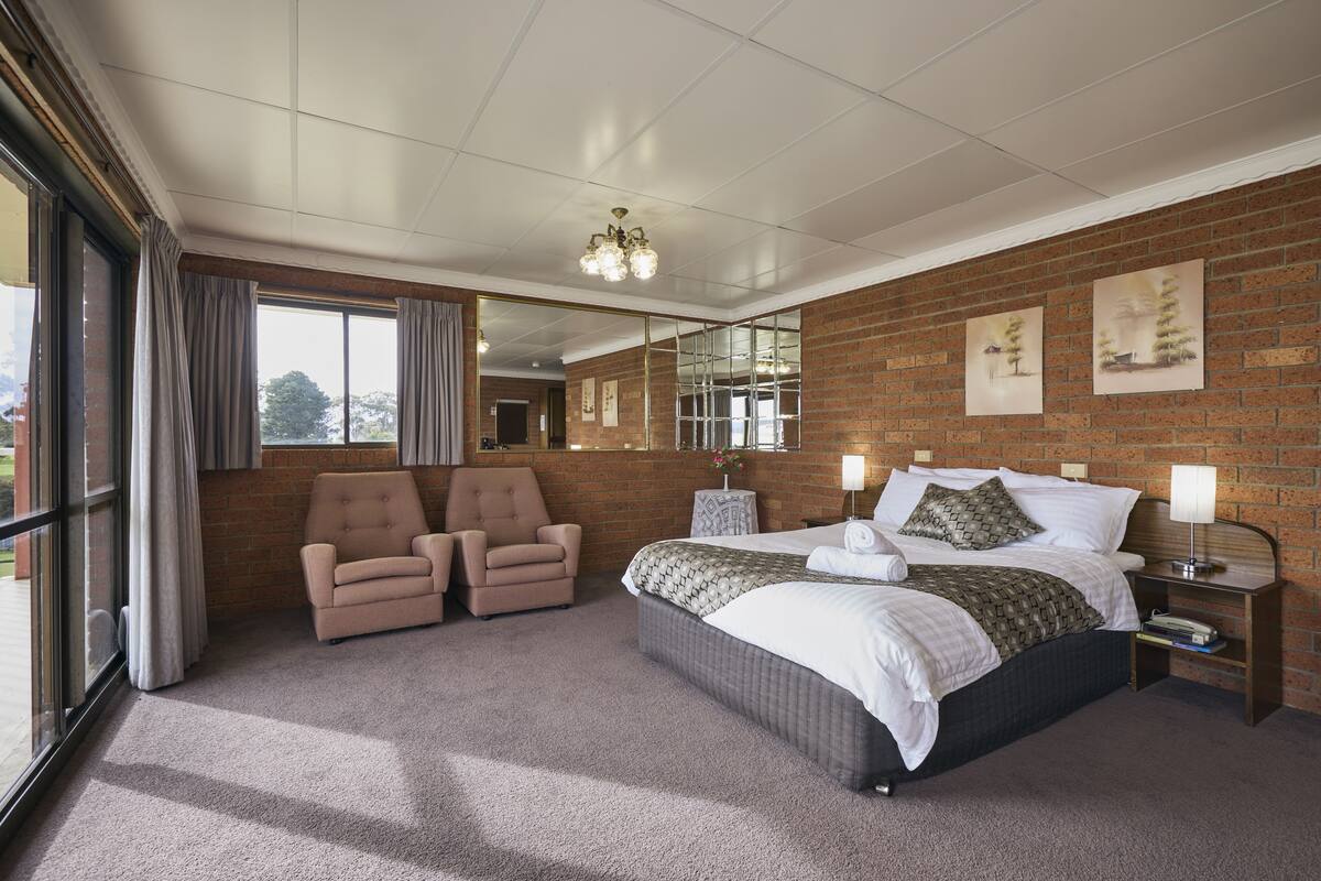 A hotel room with a large bed, two armchairs, a mirror, and a brick wall.