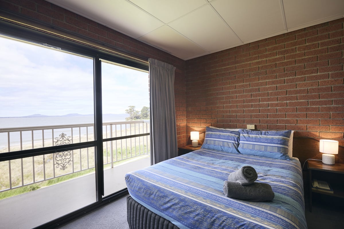 A bedroom with a large window, a bed with striped bedding, and a view of the outdoors.