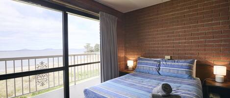 A bedroom with a large window, a bed with striped bedding, and a view of the outdoors.