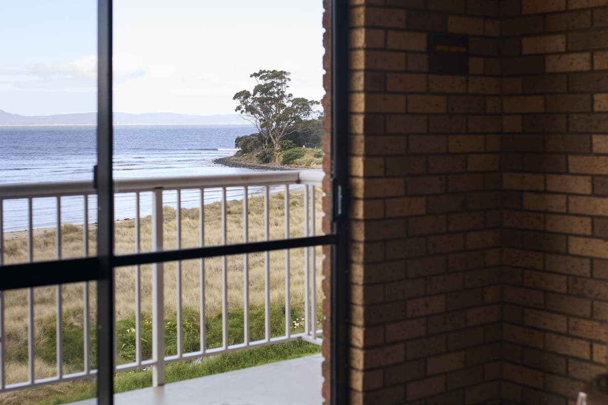 A room with a view of the sea through a glass door, a bed with a blanket, and a brick wall.