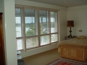 Un dormitorio con un ventanal grande, una cama de madera, una mesita de noche y una lámpara.