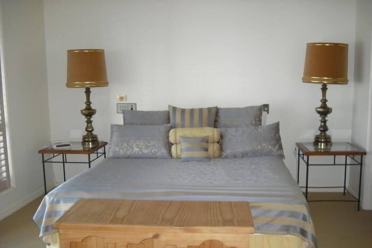 Een slaapkamer met een bed, twee nachtkastjes, twee lampen en een houten dressoir.