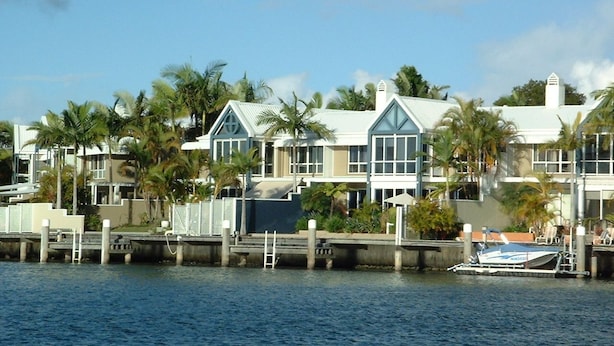 A waterfront property with a dock, a boat, and a house with large windows and a gabled roof.