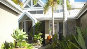 A residential building with a tiled patio, surrounded by various tropical plants and a palm tree.