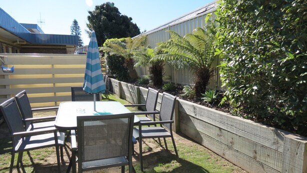 Eine Terrasse im Freien mit Tisch und Stühlen, umgeben von einem Holenzaun und üppigem Grün.