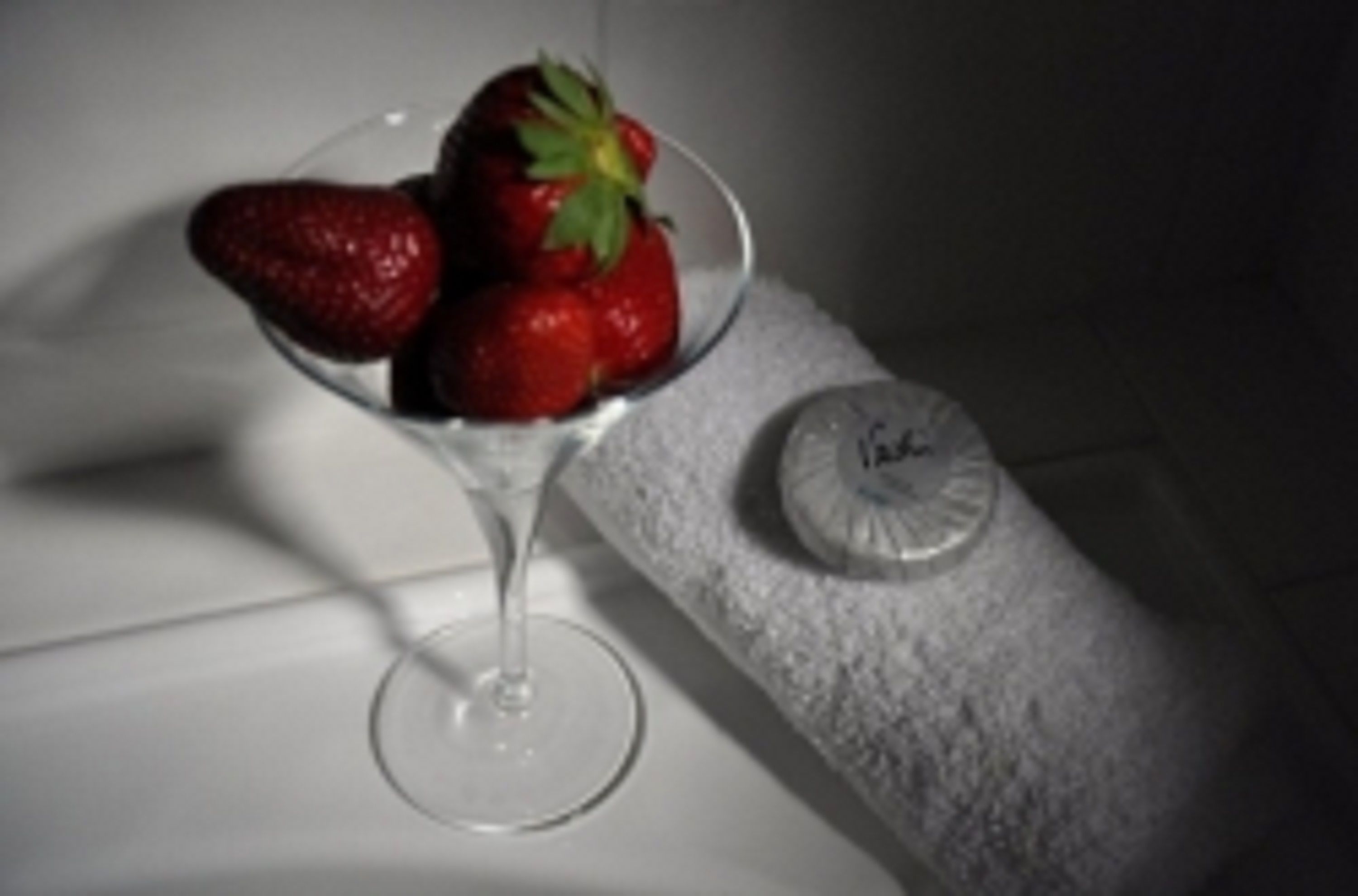A martini glass with two strawberries on a white surface.