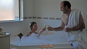 Una pareja en una bañera con velas, una copa de champán y una flor en el cabello de la mujer.