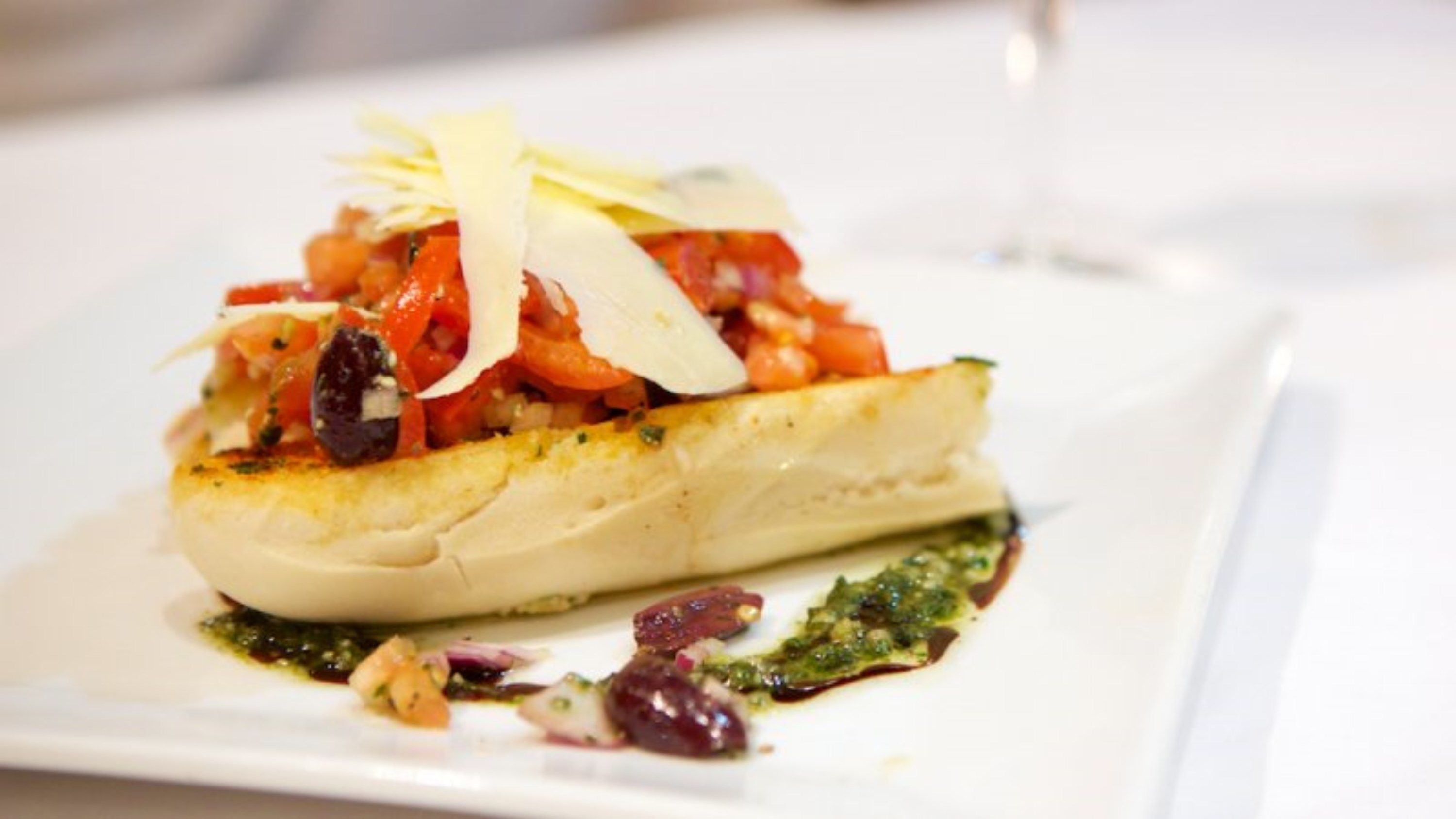A dish with a fish fillet, tomatoes, and olives on a white plate.