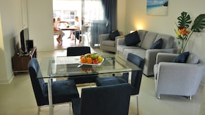 Una sala de estar moderna con una mesa de centro de vidrio, sofás grises y un comedor con una mesa y sillas.