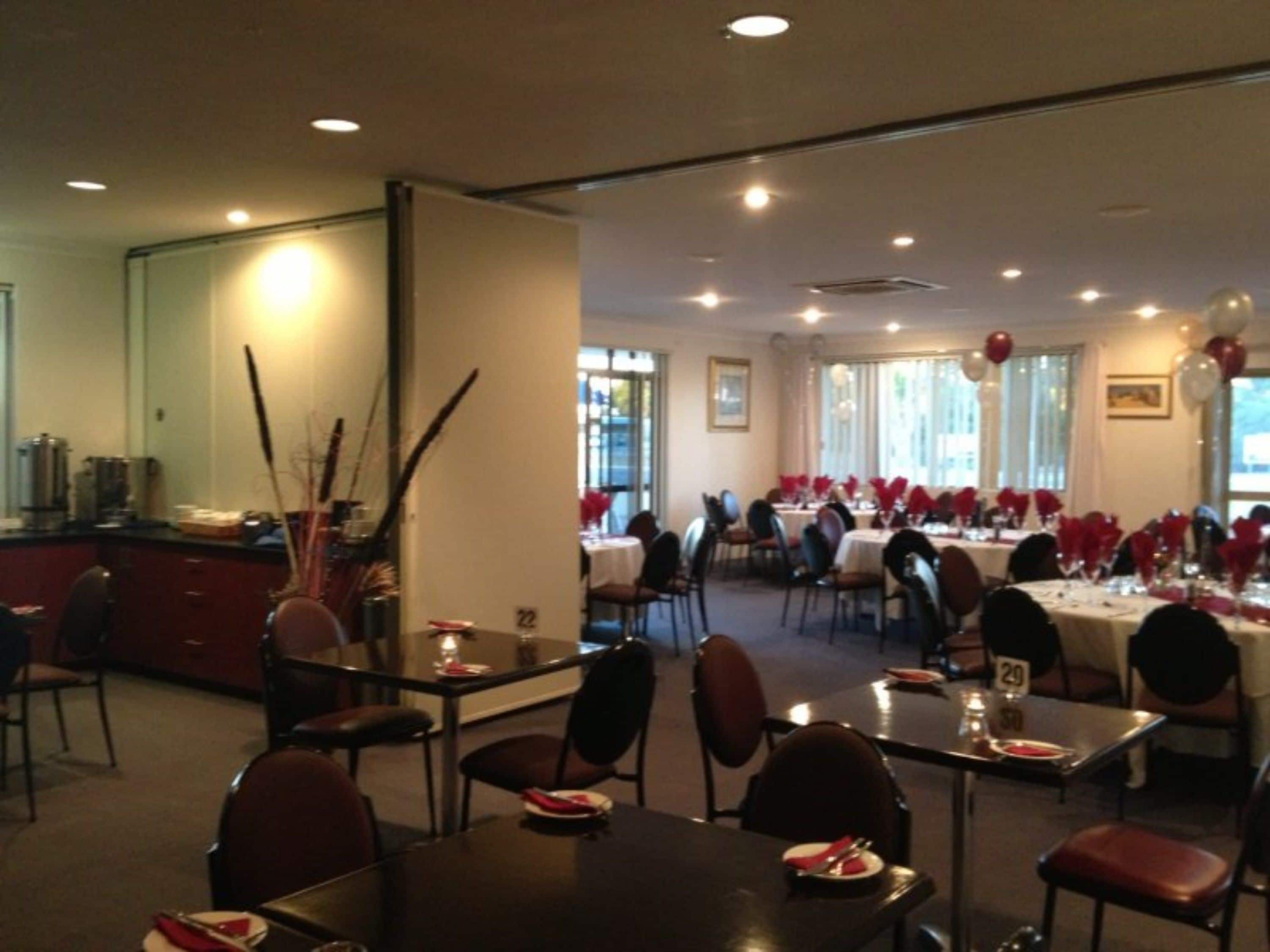 A dining area with tables set for a meal, chairs, and a counter with kitchen equipment.