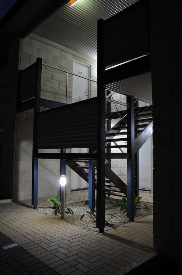 A building with a staircase, a garage door, and a small garden area with a light post.