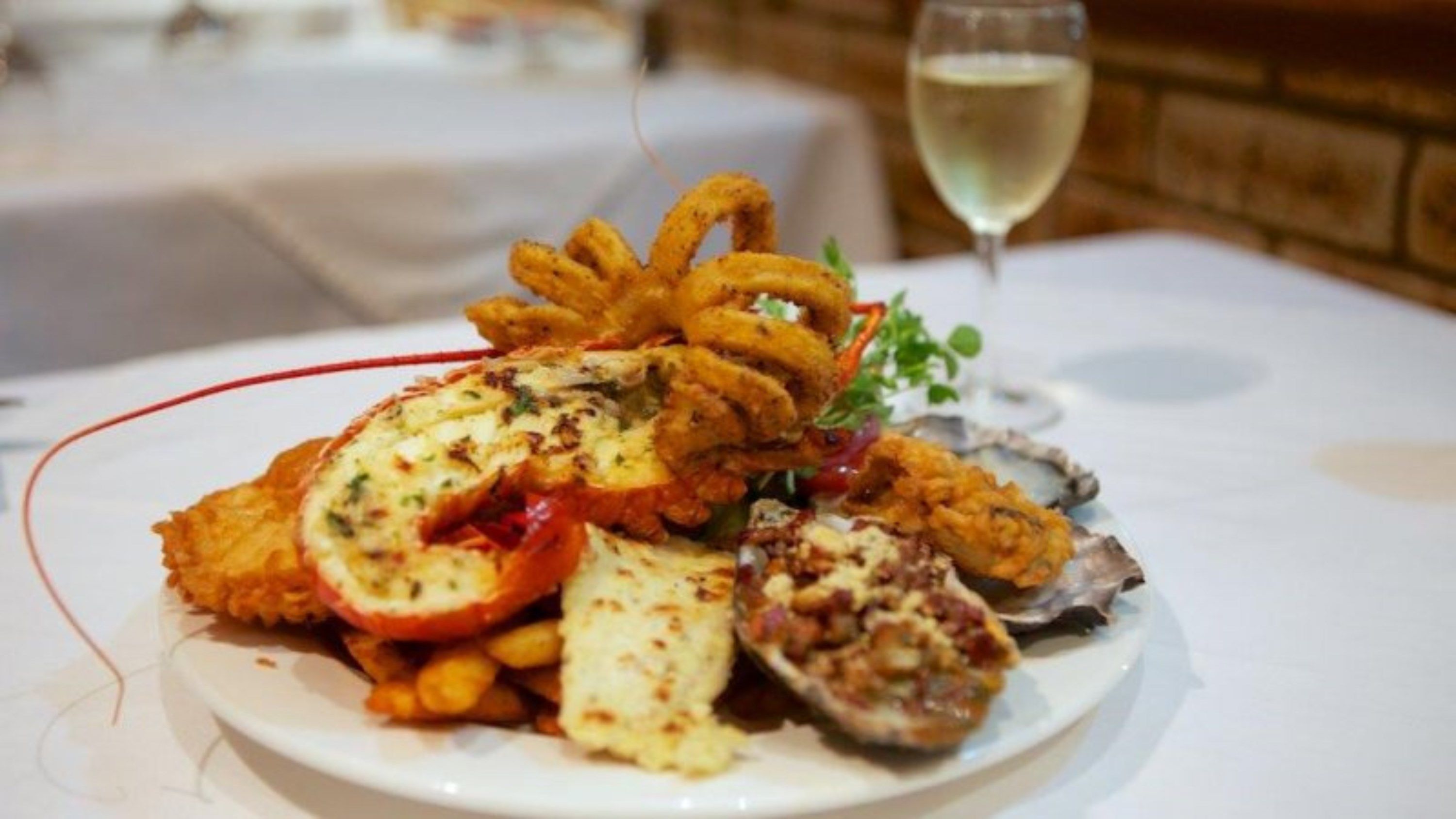 Eine Platte mit Meeresfrüchten, darunter frittierter Fisch, Austern und eine Tomatenscheibe, serviert auf einem weißen Teller.