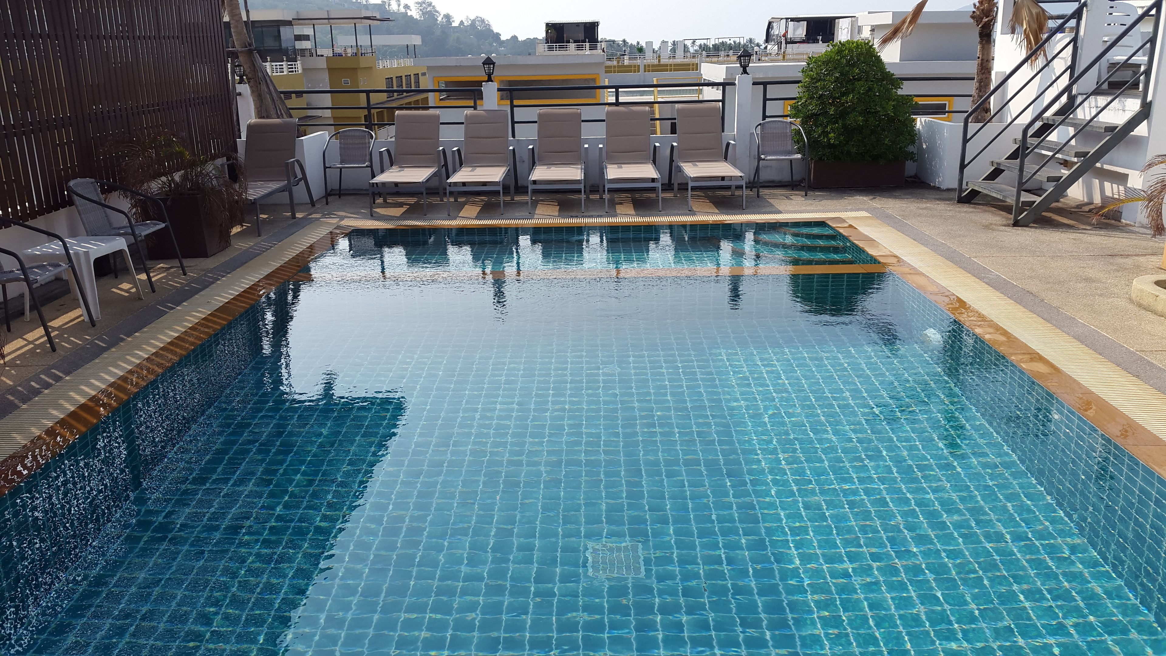 A swimming pool with tiled flooring and a surrounding area with lounge chairs and a staircase.