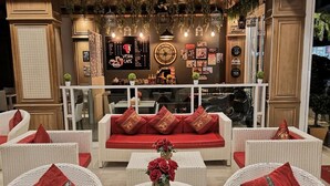 A cozy lounge area with wicker furniture and red cushions, a central coffee table with flowers, and a wall menu for a cafe. - Patong Princess (Patong)
