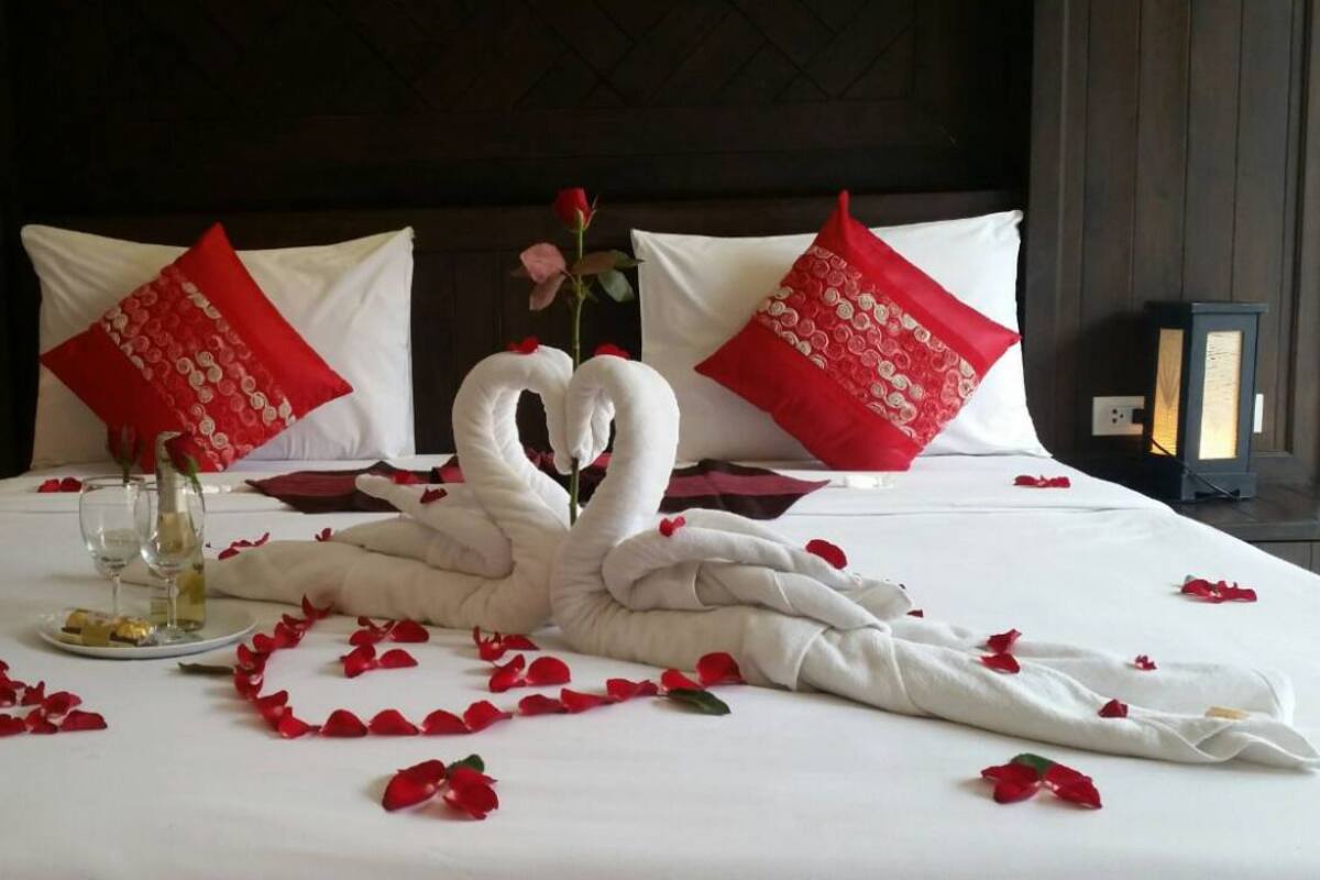 A bed with a heart-shaped swan decoration made of towels, red rose petals, and a single rose.