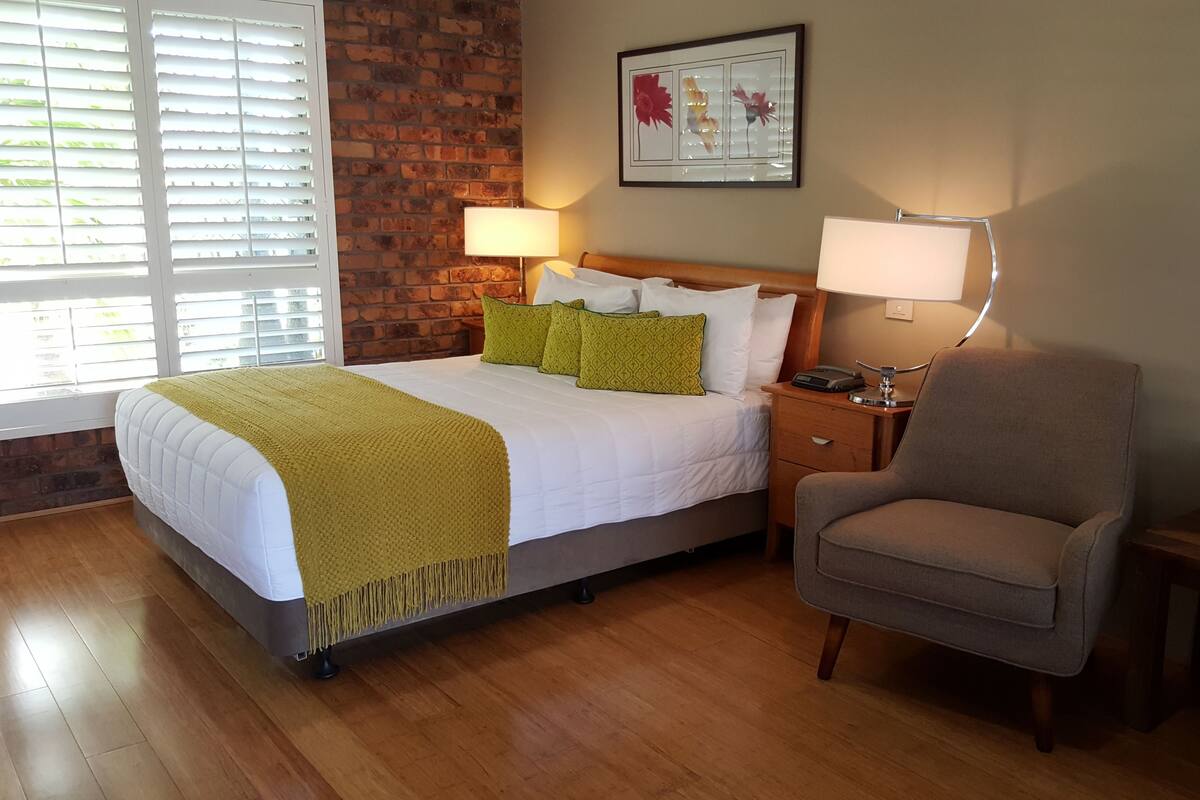 Ein Hotelzimmer mit einem Bett, einem Sessel, einem Nachttisch und einem Wandbild.