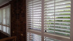 A room with a brick wall, a window with white blinds, and a wooden railing. - Ballina Palms Boutique Motel (Ballina)