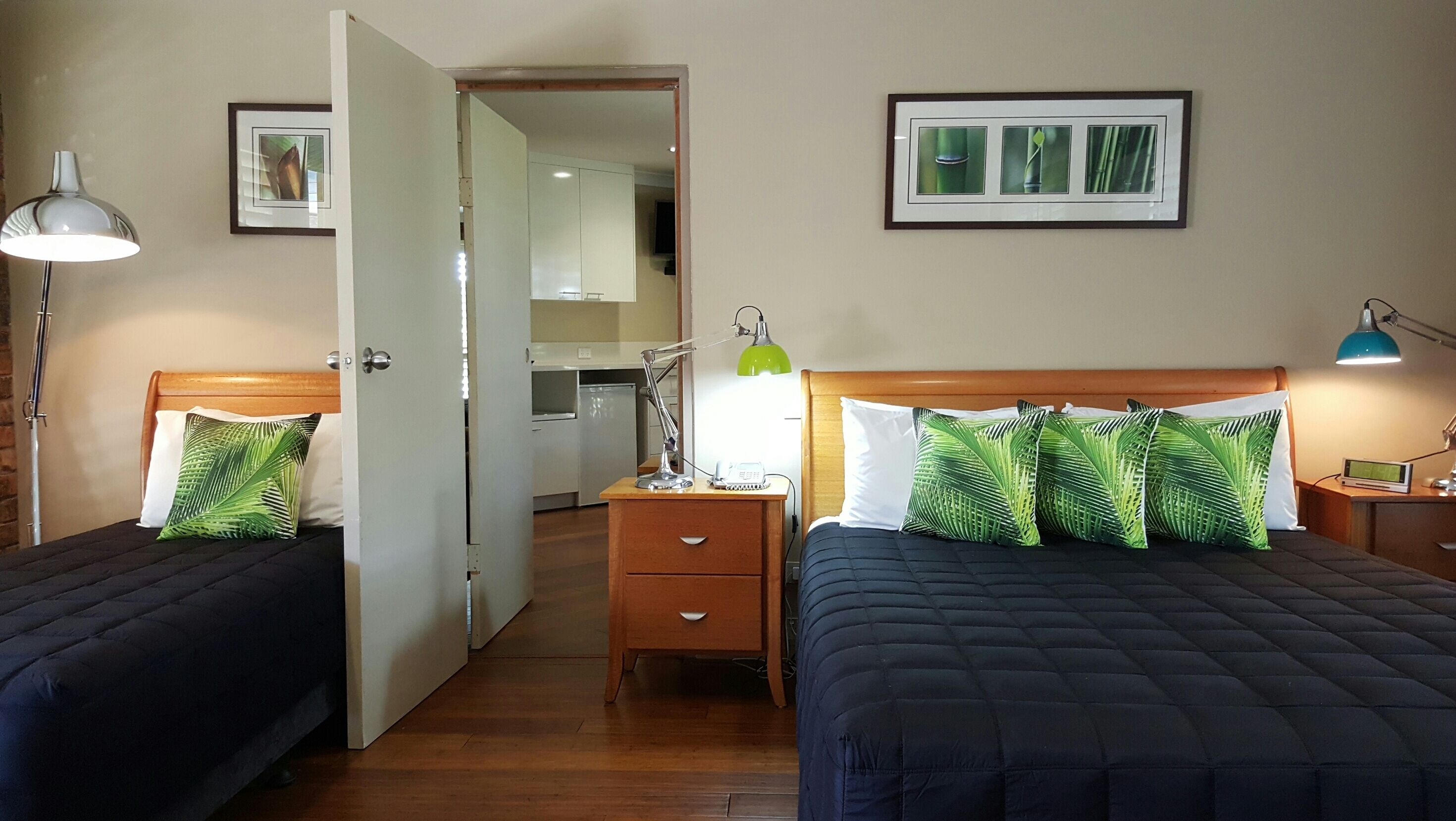 A hotel room with two beds, a nightstand with a lamp, a small desk with a lamp, and a framed picture on the wall.