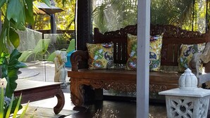 A wooden bench with colorful cushions, a white lantern, and tropical plants. - Ballina Palms Boutique Motel (Ballina)