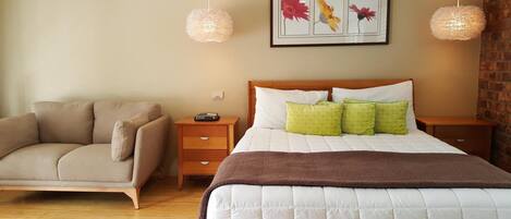 Un dormitorio con una cama, una silla, dos mesitas de noche, un buró, un cuadro enmarcado y dos lámparas colgantes.