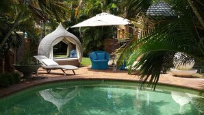 A pool area with a lounge chair, a blue chair, and a covered seating area. - Ballina Palms Boutique Motel (Ballina)