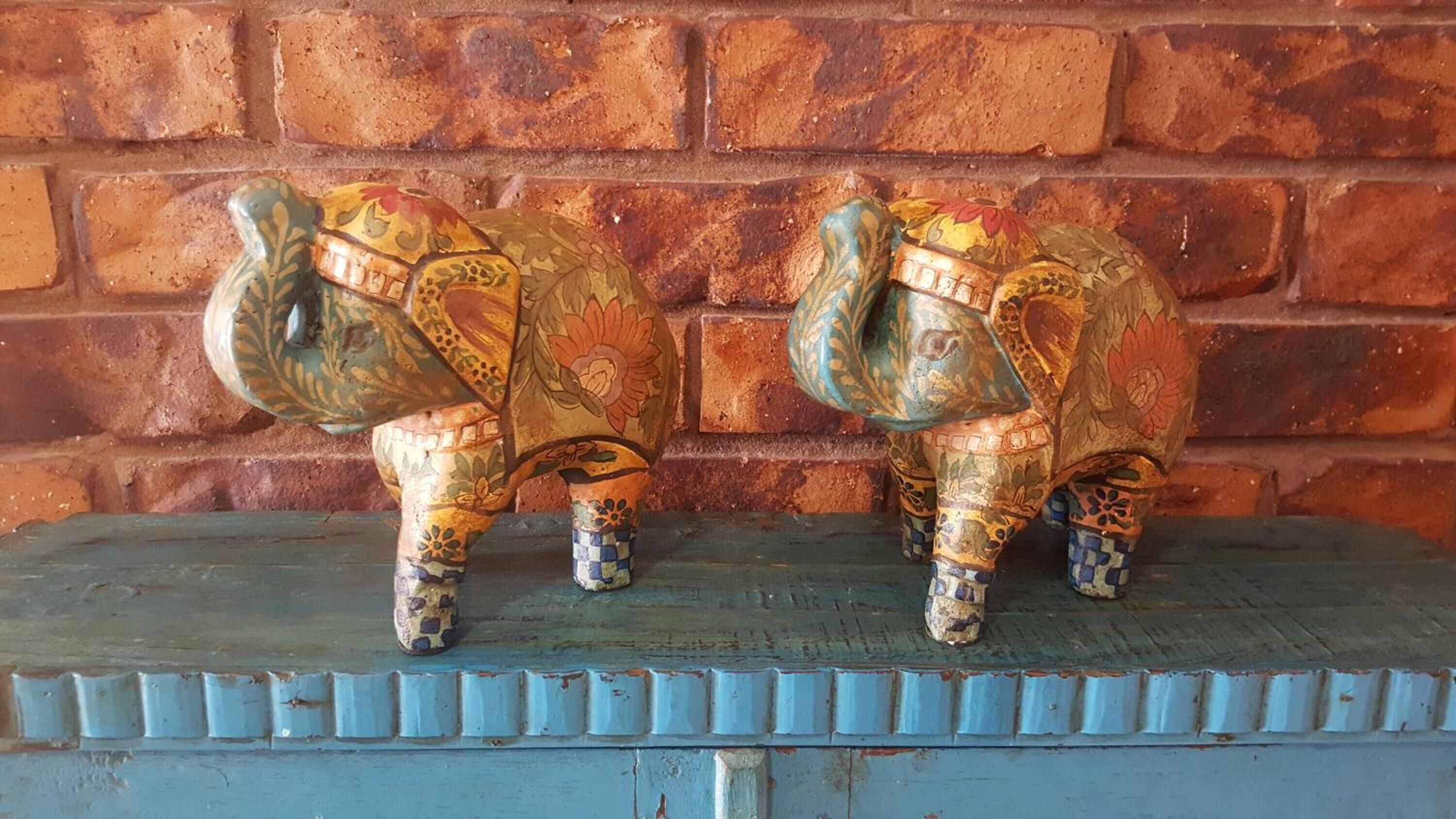 Two ceramic elephant sculptures on a blue-painted shelf against a brick wall.