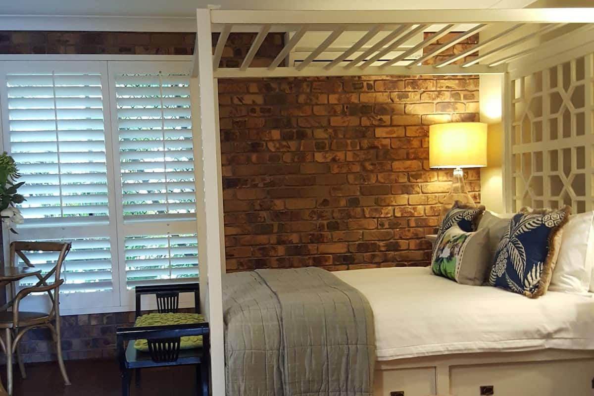 Ein Schlafzimmer mit Bett, Deckenventilator, Backsteinwand, Fenster mit Jalousien und Holzboden.