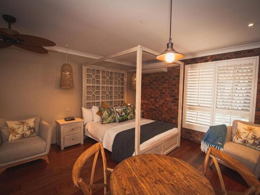 A bedroom with a four-poster bed, a wooden ceiling fan, a hanging light fixture, and a brick wall.