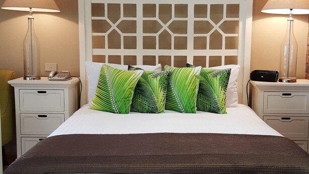 A neatly made bed with a patterned headboard, two bedside tables with lamps, and a wooden floor. - Ballina Palms Boutique Motel (Ballina)