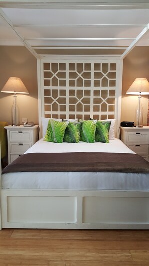 A neatly made bed with a patterned headboard, two bedside tables with lamps, and a wooden floor. - Ballina Palms Boutique Motel (Ballina)