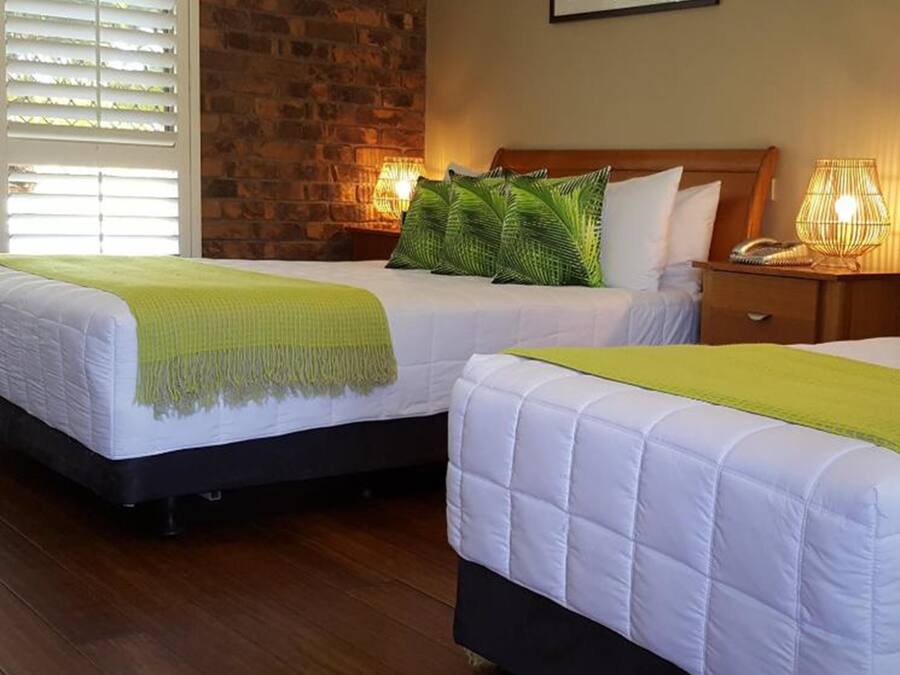 Two single beds with white bedding and green throw blankets, a brick wall, and a window with blinds.
