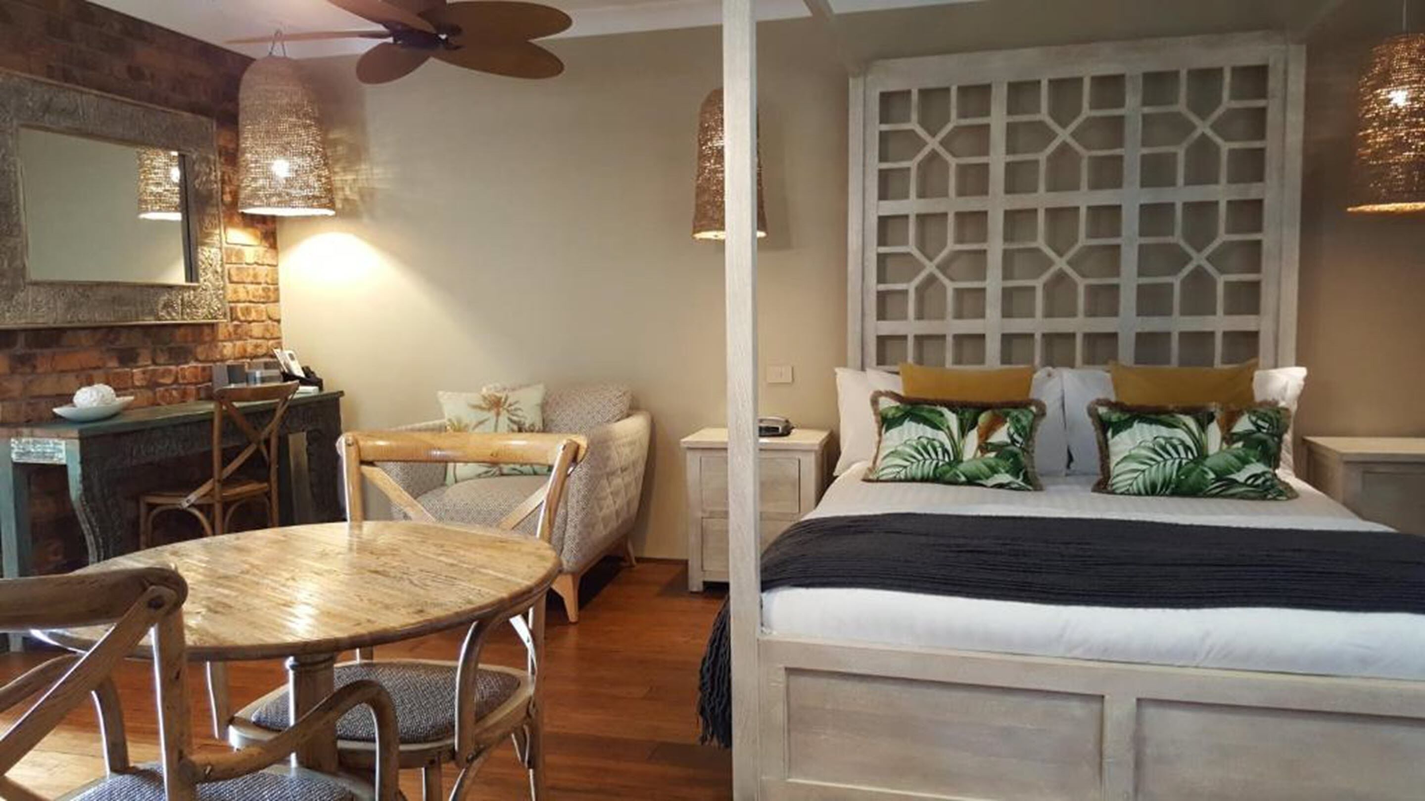 A room with a bed, a wooden table, chairs, a desk, and a decorative wall.