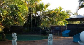 Un espace piscine agrémenté d’une statue, d’une chaise bleue et d’une clôture.
