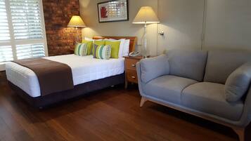 A hotel room with a bed, a sofa, two bedside lamps, a wooden nightstand, and a brick wall.