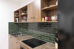 Una cocina con estufa negra, armarios de madera y salpicadero con azulejos verdes.