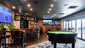 Een barruimte met een pooltafel, zitplaatsen en een televisiescherm waarop een sportevenement wordt vertoond.