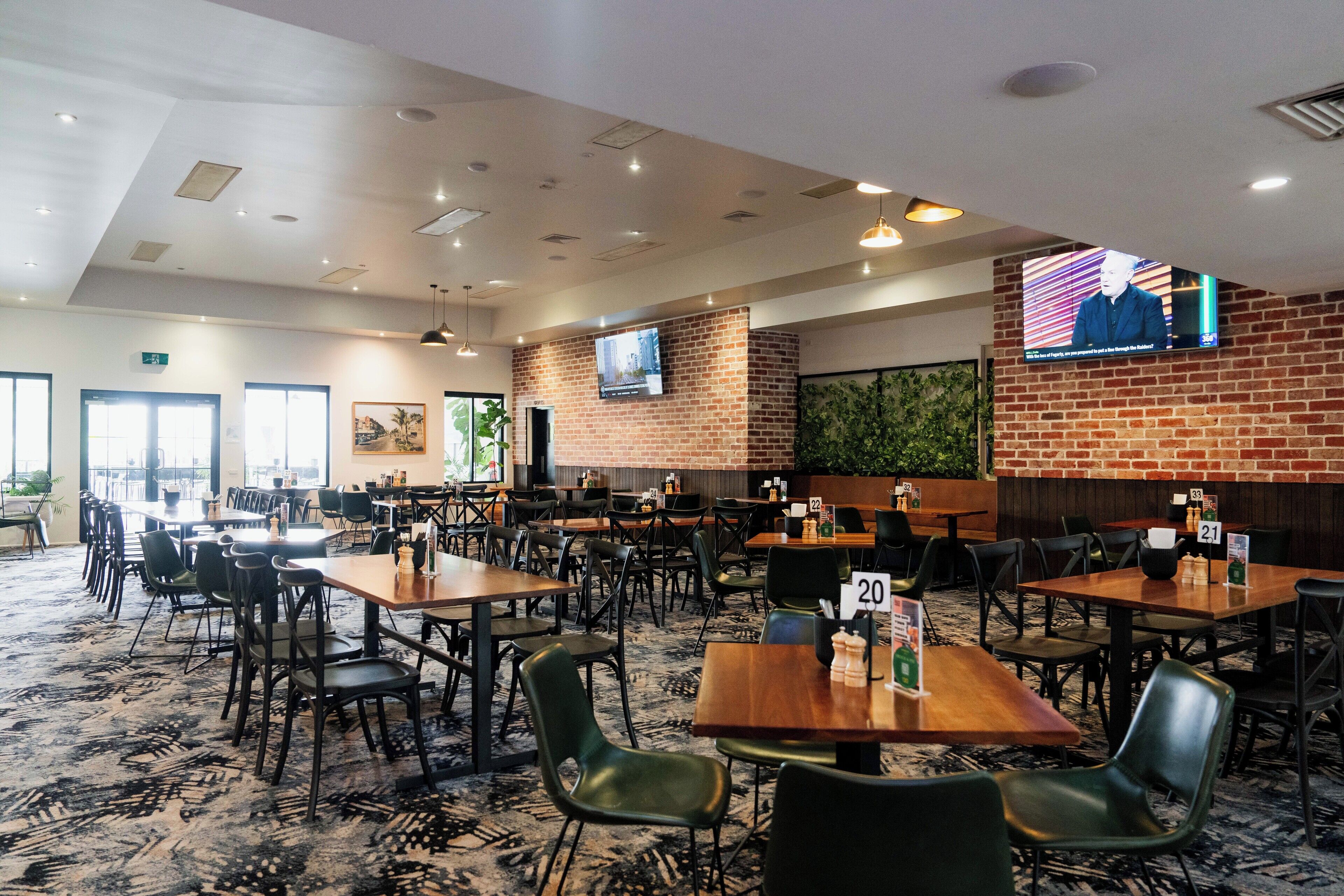 Un grand espace dédié à la salle à manger, avec plusieurs tables et chaises, un mur en briques et un écran de télévision fixé au mur.