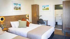 Een hotelkamer met twee bedden, een bureau en een douche.