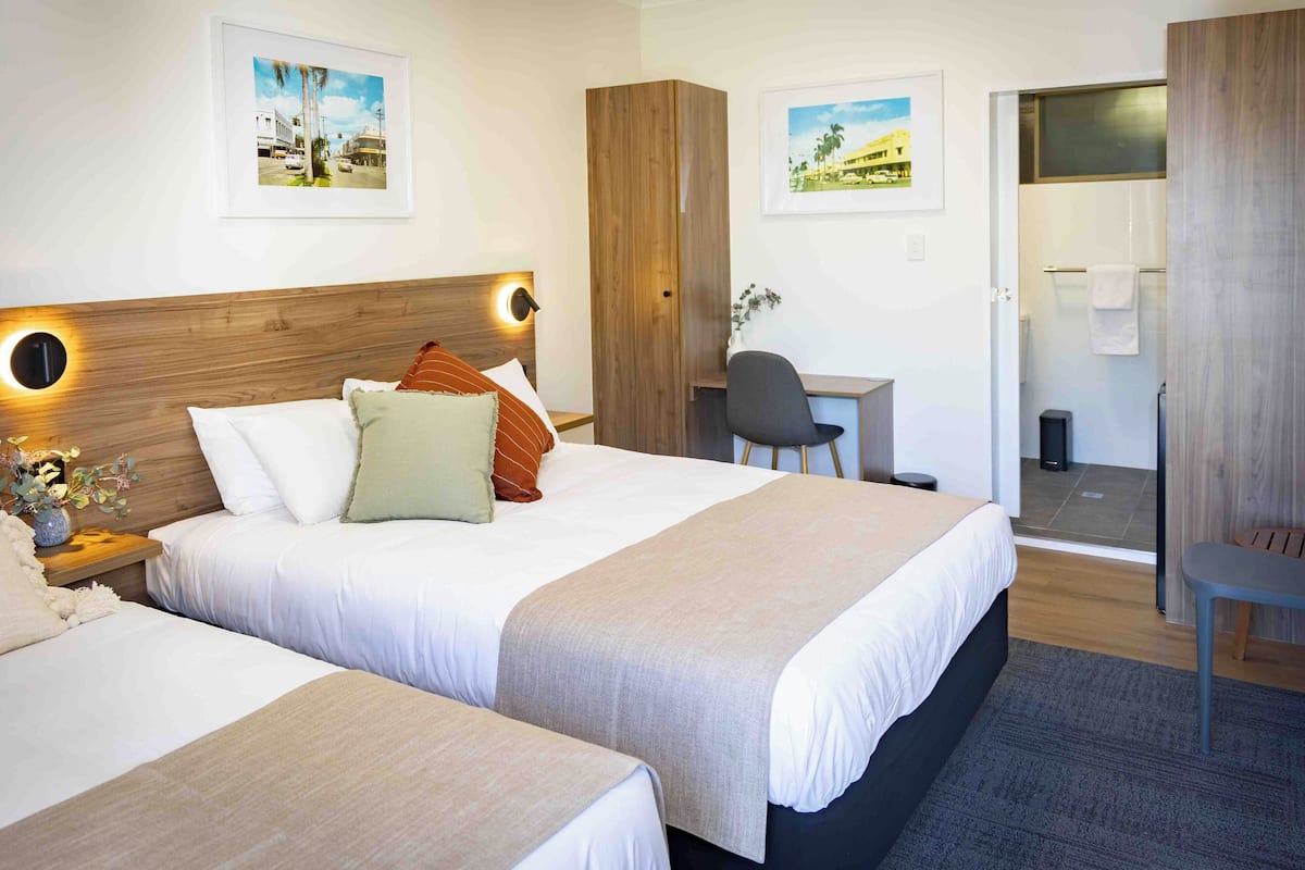 A hotel room with two beds, a desk, and a shower area.
