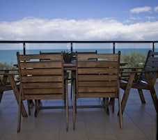 Una mesa y sillas de madera en un balcón con vista al océano.