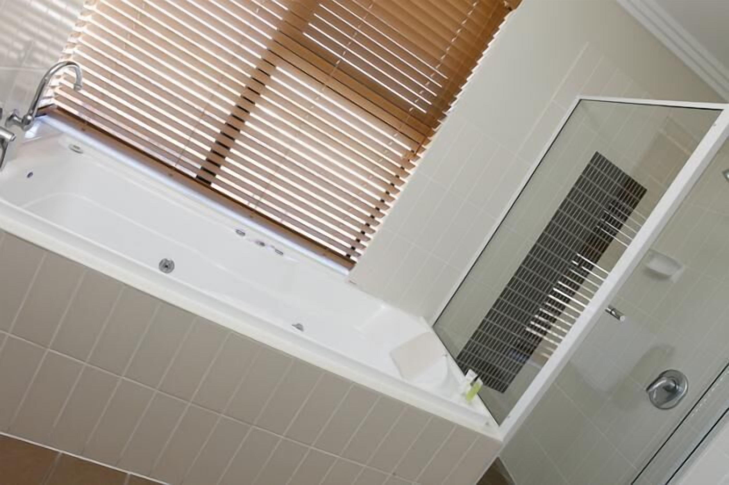 Een badkamer met een bad, een douche en een raam met zonwering.