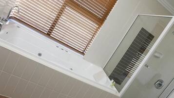 Een badkamer met een bad, een douche en een raam met zonwering.