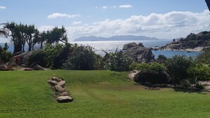 A view of a grassy area with rocks and trees, leading to a body of water with mountains in the distance. - Whitsunday Sands Resort (Bowen)